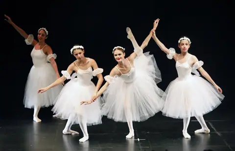 Vier jugendliche Ballerinas in langen weißen Tüllröcken und Blumenkränzen, eine hebt ein Bein hoch