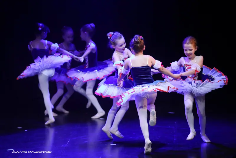Jeunes ballerines en tutus bleu marine et blanc se tiennent la main et tournent en rondes sous une lumière violette