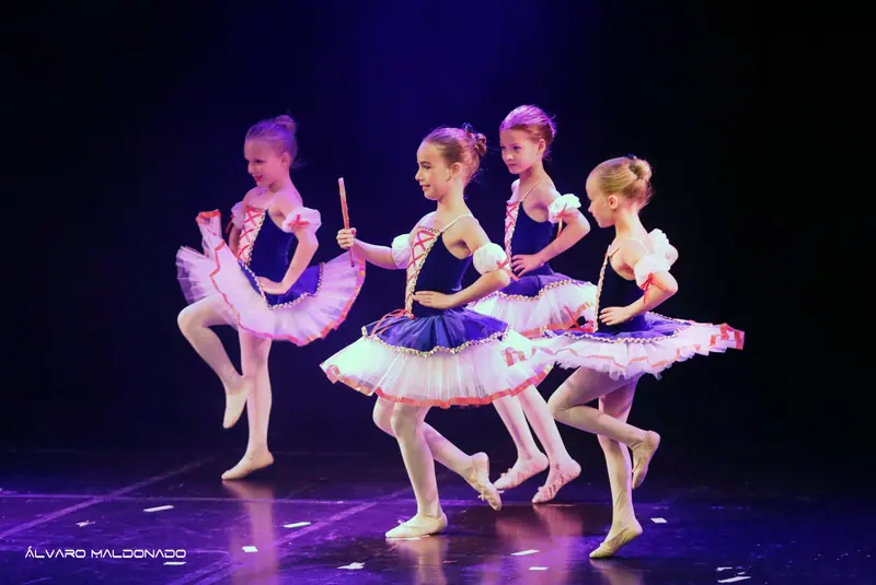 Quatre jeunes ballerines en tutus bleu marine et blanc à laçage rouge sautillent sur un pied, mains sur les hanches