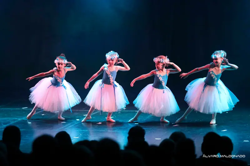 Quatre fillettes en longs tutus blancs et couronnes de fleurs fléchissent de côté, une main près de la tête, scène bleue