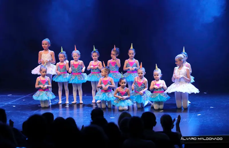 Des fillettes en tutus turquoise à sequins et chapeaux pointus, à genoux ou debout près de deux grandes en tutu blanc