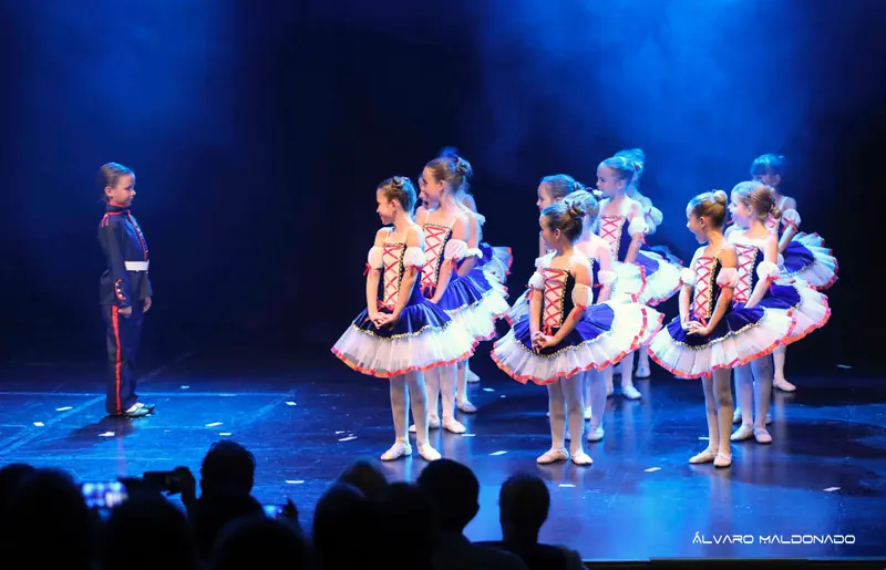 Un garçon en uniforme de soldat bleu marine face à un groupe de filles en tutus bleu marine et blanc à laçage rouge