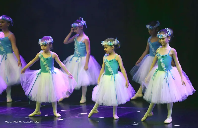 Jeunes danseuses en turquoise et longs tutus blancs, couronnes de fleurs, marchent pointe tendue sur une scène sombre
