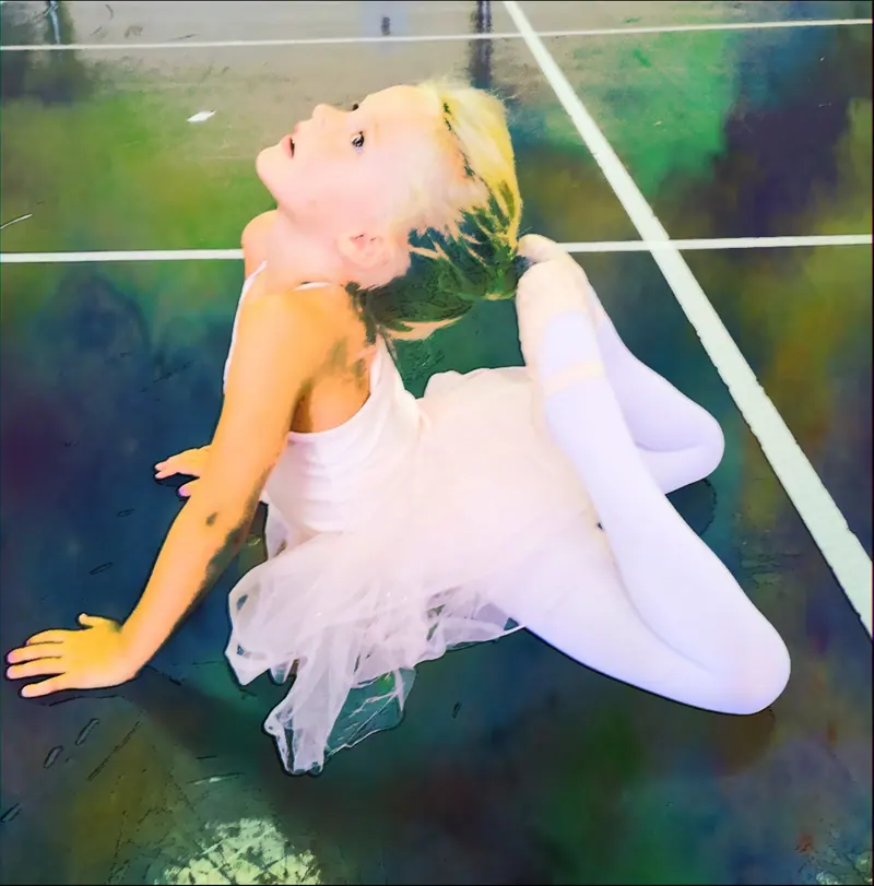 Une fillette blonde en tutu rose, assise au sol, se cambre pour toucher sa tête avec son pied, filtre coloré