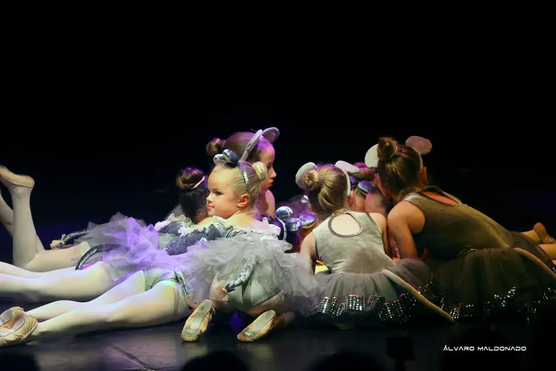 De petites filles en costumes de souris grise aux oreilles rondes sont allongées sur le ventre, serrées sur scène