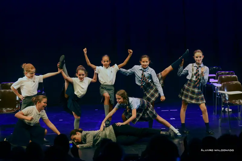 Des filles en uniforme scolaire, jupes écossaises et cravates, lancent la jambe et exultent sur une scène éclairée en bleu