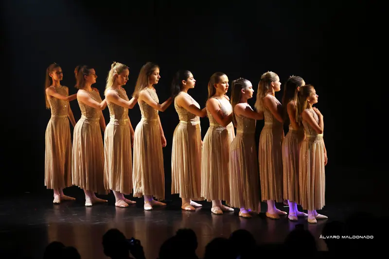 Une file de danseuses adolescentes en longues robes dorées pailletées, de profil, la main sur l’épaule de celle de devant