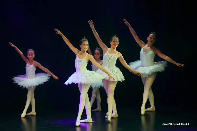 Des danseuses souriantes en tutus classiques blancs et diadèmes lèvent un bras en diagonale, certaines sur pointes