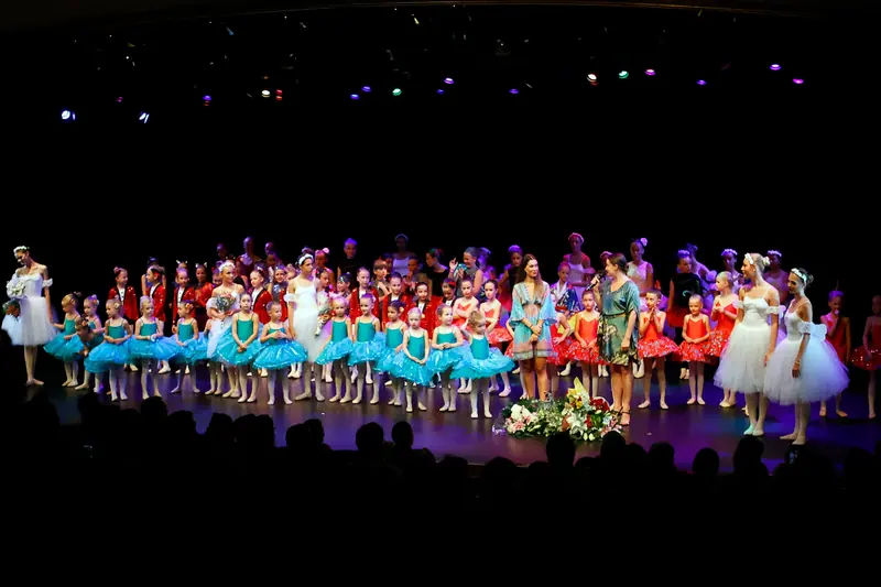 Toute la troupe alignée pour le salut final, les plus jeunes en tutus turquoise devant et des bouquets sur scène
