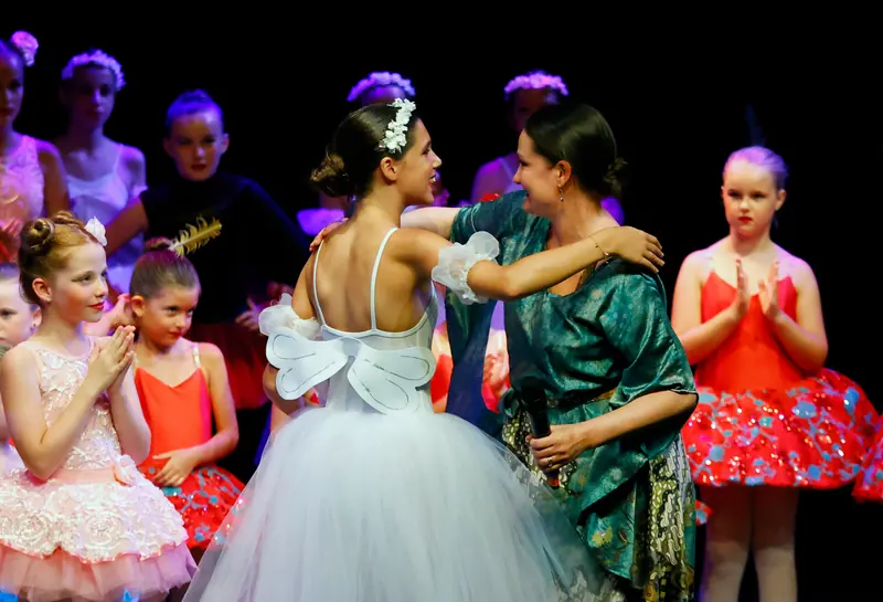 Une femme en tunique de soie verte, micro à la main, serre dans ses bras une danseuse en tutu blanc sous les applaudissements