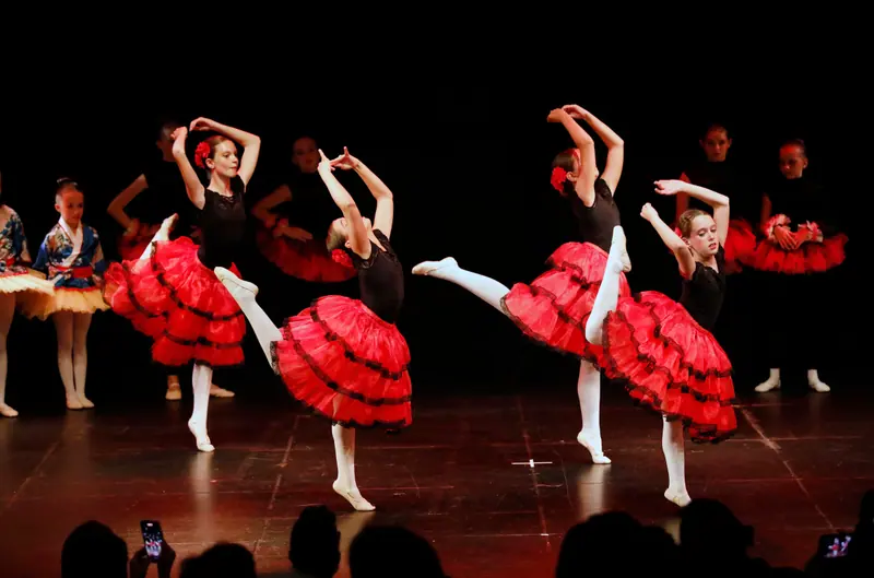 Des filles en justaucorps noir et tutu rouge à volants, fleurs rouges dans les cheveux, se cambrent une jambe levée