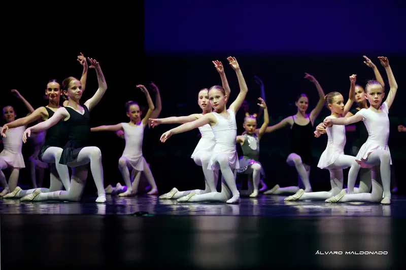 Élèves de ballet en justaucorps blancs et noirs à genou, un bras levé et l'autre tendu vers l'avant