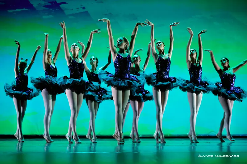 Danseuses en tutus bleu foncé à sequins montent sur demi-pointes, bras tendus vers le haut, devant un fond vert turquoise