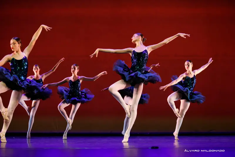 Danseuses en tutus bleu foncé à sequins en équilibre sur une jambe, l'autre genou plié, bras ouverts, devant un fond rouge