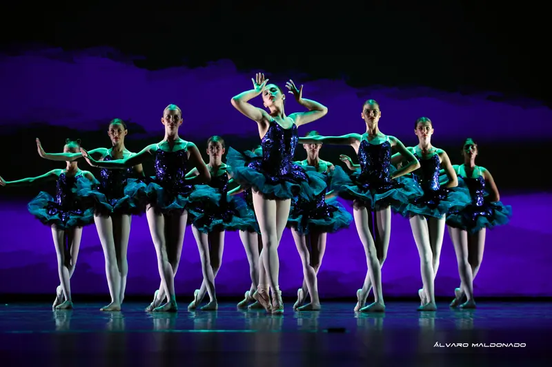 Danseuses adolescentes en tutus bleu foncé à sequins en formation, la soliste sur pointes encadrant son visage de ses mains