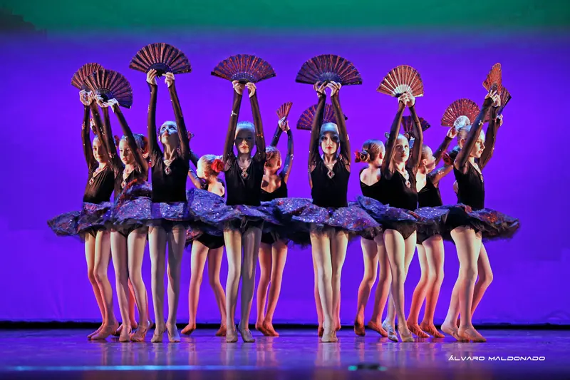 Fillettes en justaucorps de velours noir et tutus scintillants tenant des éventails rouges et noirs au-dessus de la tête sous lumière violette