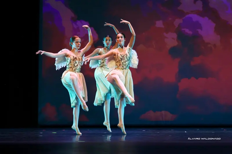 Trois fillettes à ailes d'ange et bustiers dorés à sequins sur une jambe, genou levé, devant des nuages rouges et violets