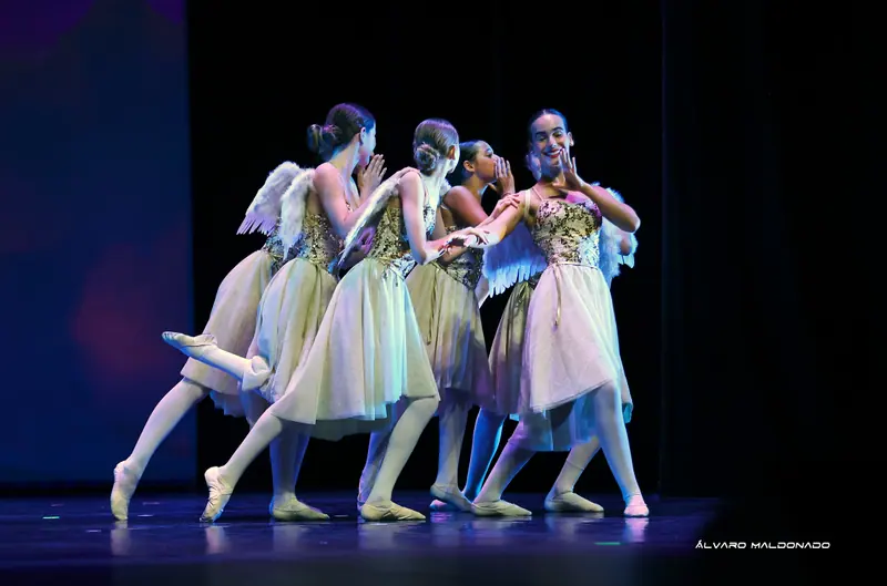 Danseuses à ailes d'ange et robes crème chuchotant et riant ensemble dans une scène espiègle sur une scène sombre