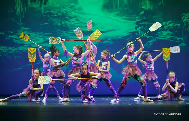 Fillettes en combinaisons à motifs colorés et tutus violets posant avec des pagaies peintes devant une projection de rivière verte