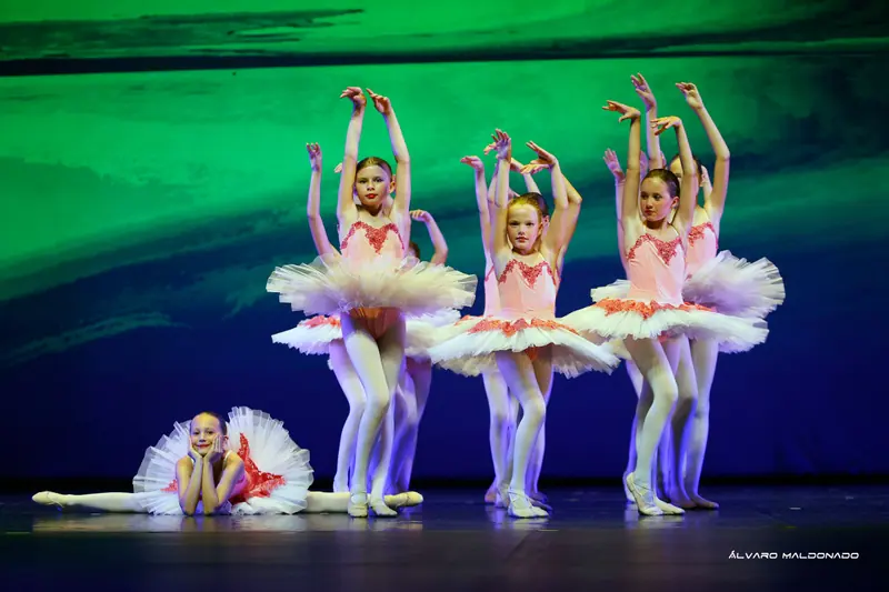 Fillettes en tutus roses et blancs, bras au-dessus de la tête, tandis qu'une fillette souriante fait le grand écart, menton dans les mains