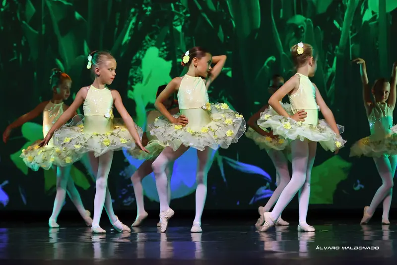 Petites filles en tutus jaune pâle ornés de fleurettes posant mains sur les hanches devant une projection de jungle verte