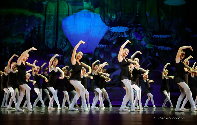 Un grand groupe en justaucorps noirs et collants blancs tient un bras arrondi au-dessus de la tête devant un décor de lanternes bleues