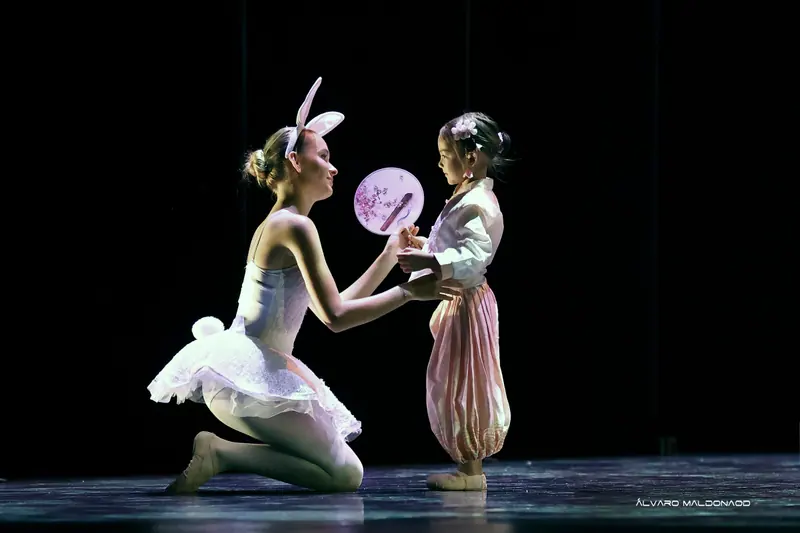 Une danseuse agenouillée en tutu blanc de lapin tend un éventail rond peint à une fillette en tenue de soie rose