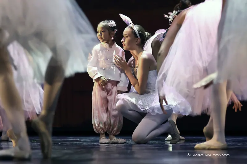 Une fillette en tenue de soie rose se tient près d'une danseuse agenouillée en tutu blanc et oreilles de lapin, parmi des tutus flous