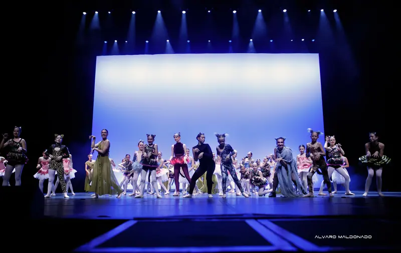 Toute la troupe en costumes d'animaux, tutus et robes danse ensemble sous des projecteurs bleus