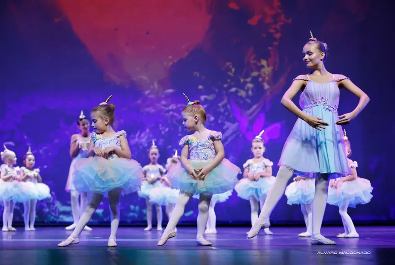 Petites filles avec serre-têtes licorne et tutus pastel à paillettes dansant près d'une danseuse plus âgée en robe lilas