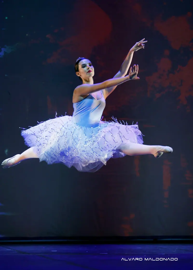 Une ballerine en tutu blanc scintillant et diadème s'envole en grand jeté sur une scène sombre
