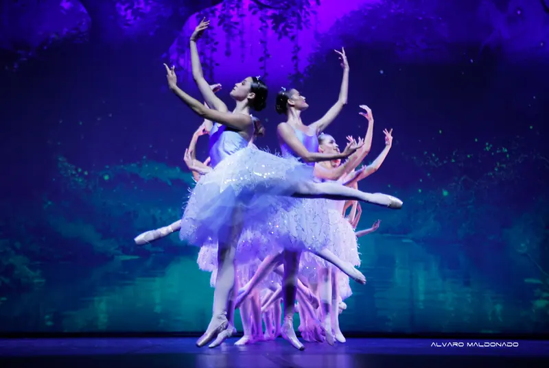 Danseuses en tutus blancs scintillants sur pointes en arabesques superposés devant une forêt bleue et violette